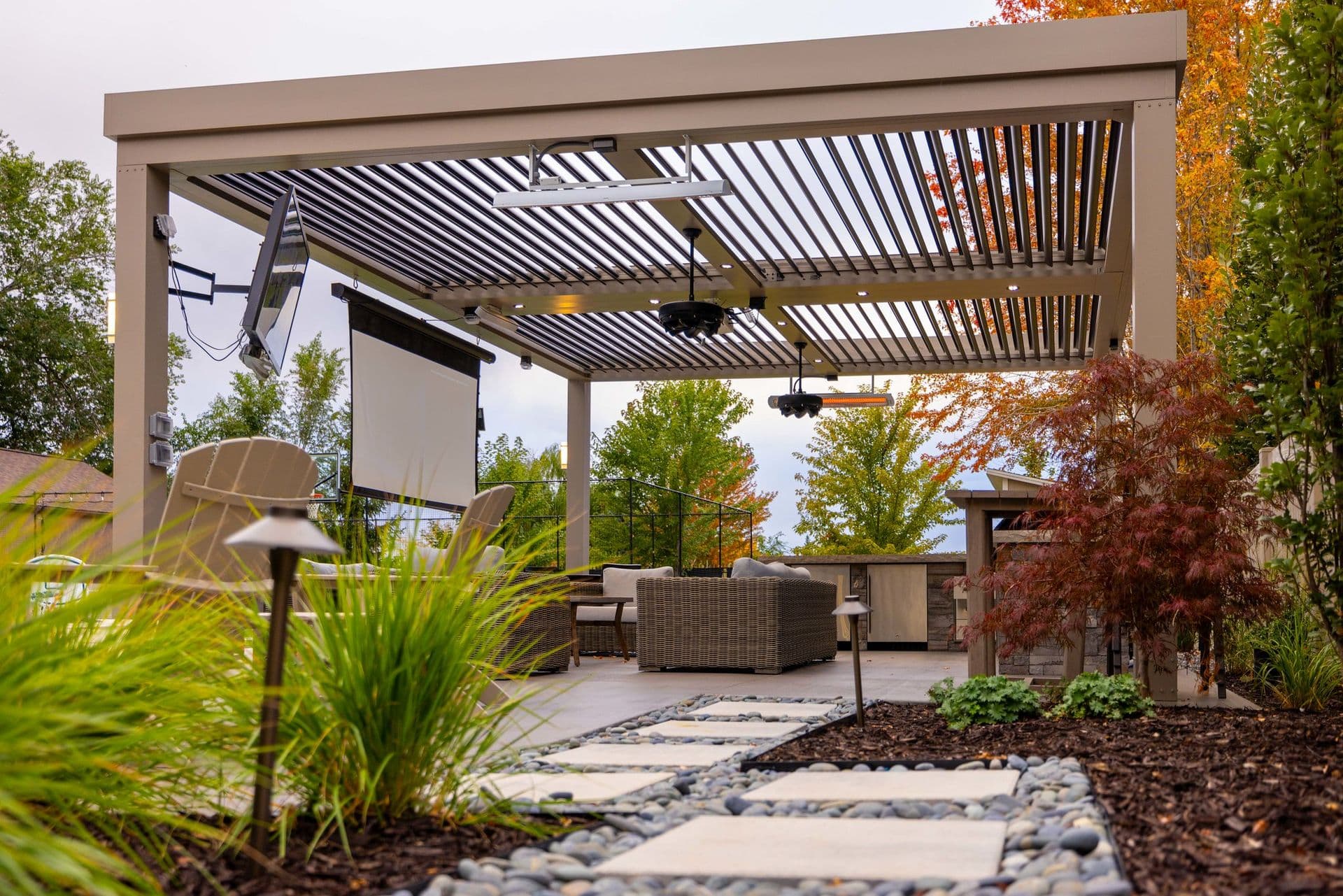 Modern pergola patio with cozy seating, surrounded by lush greenery and vibrant autumn trees. Soft lighting and a relaxed, inviting atmosphere.
