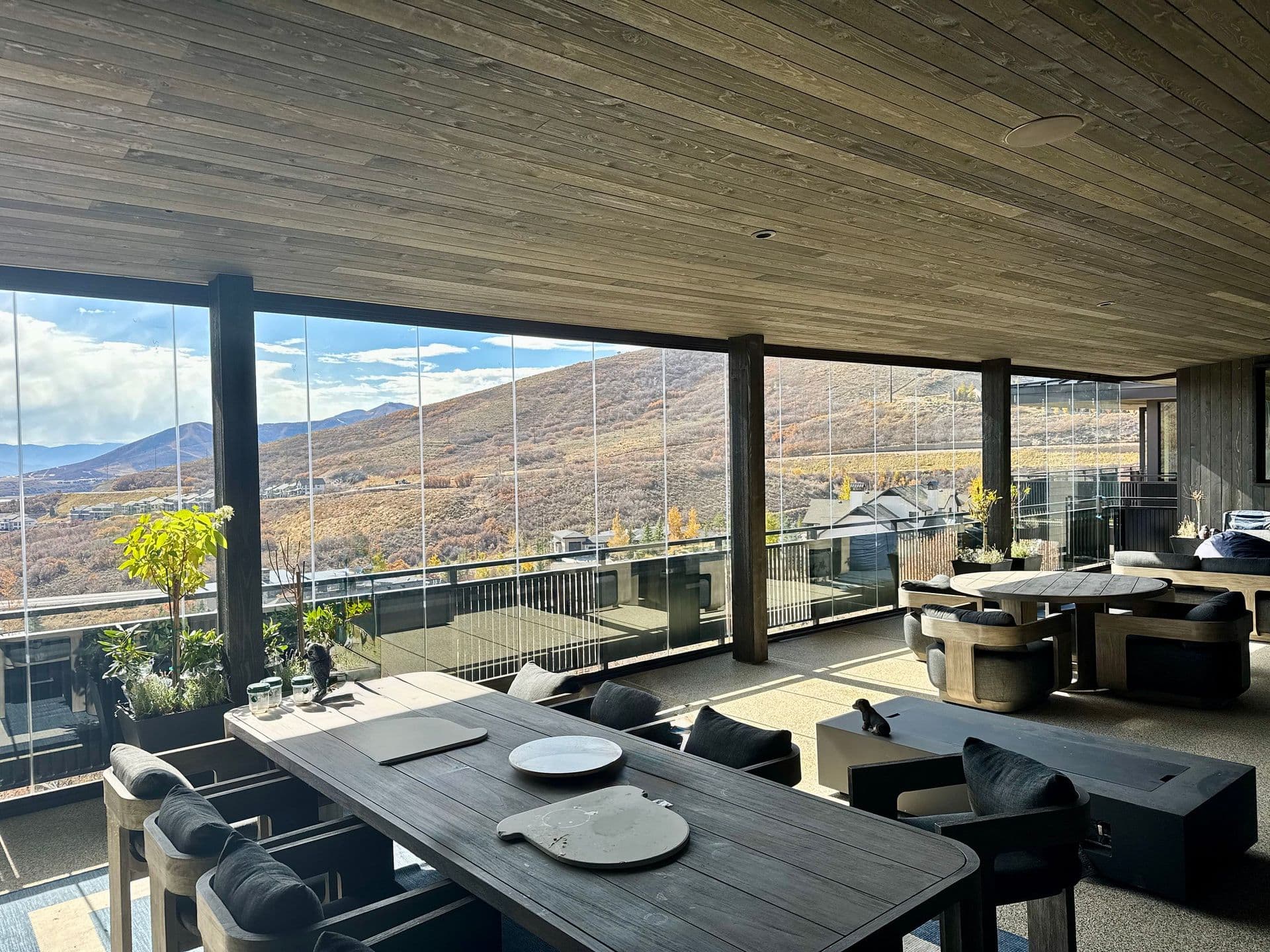 Spacious room with wood ceiling, large windows showcasing mountain views. Modern furniture and plants add a cozy, stylish ambiance.