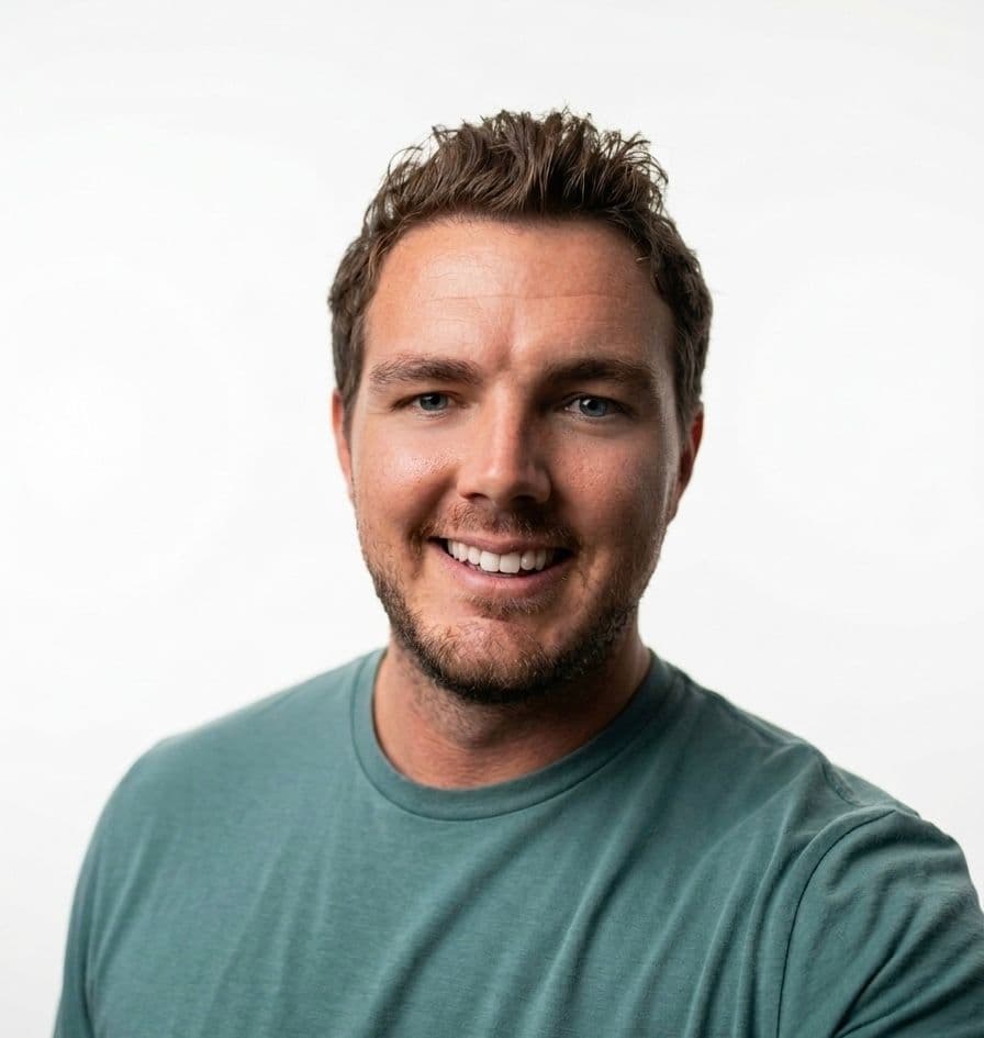 Smiling man with short hair wearing a teal shirt against a plain white background. The image conveys a friendly and approachable vibe.